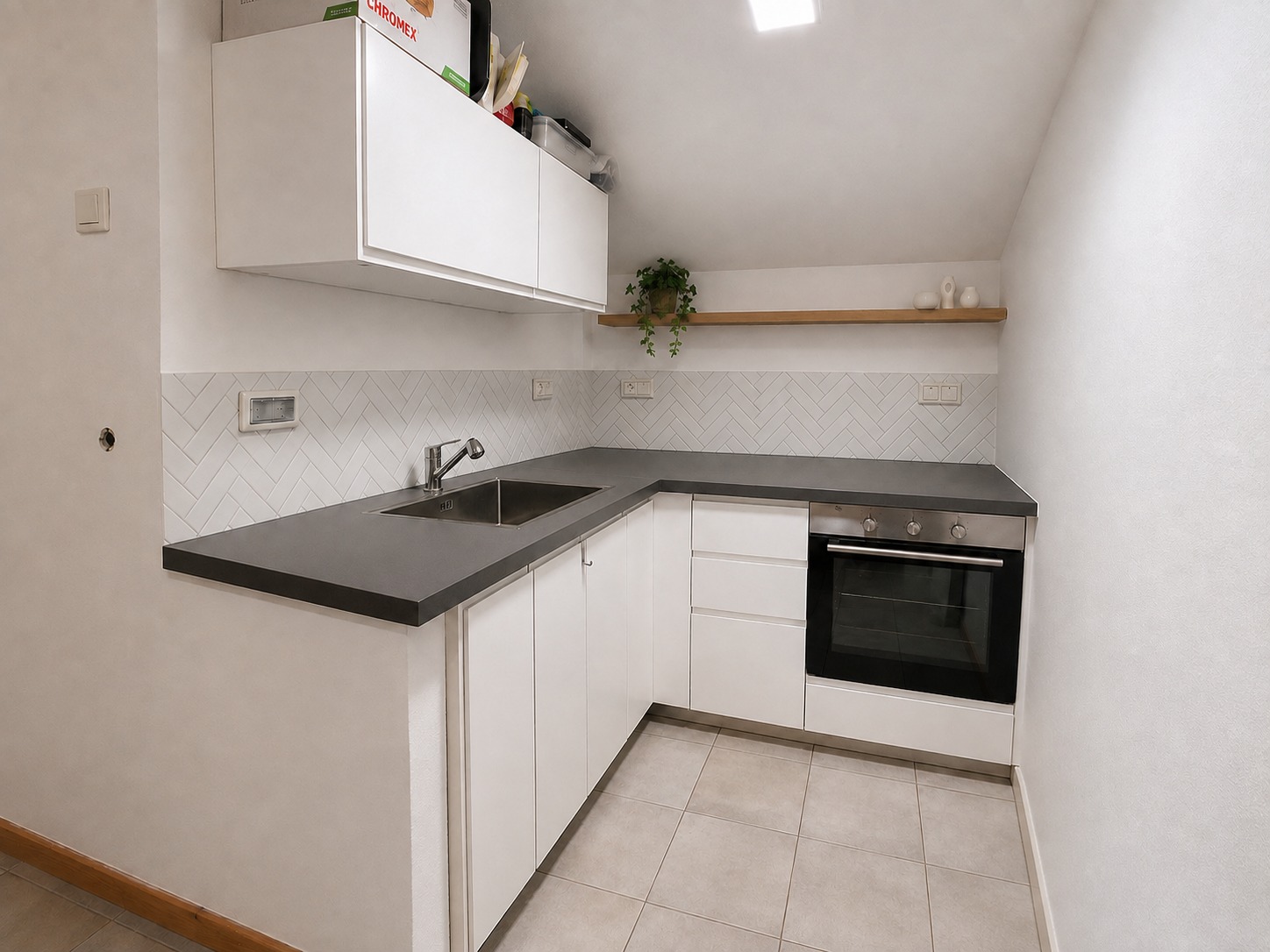 Compact kitchen with white cabinetry, herringbone tile and a floating wood shelf